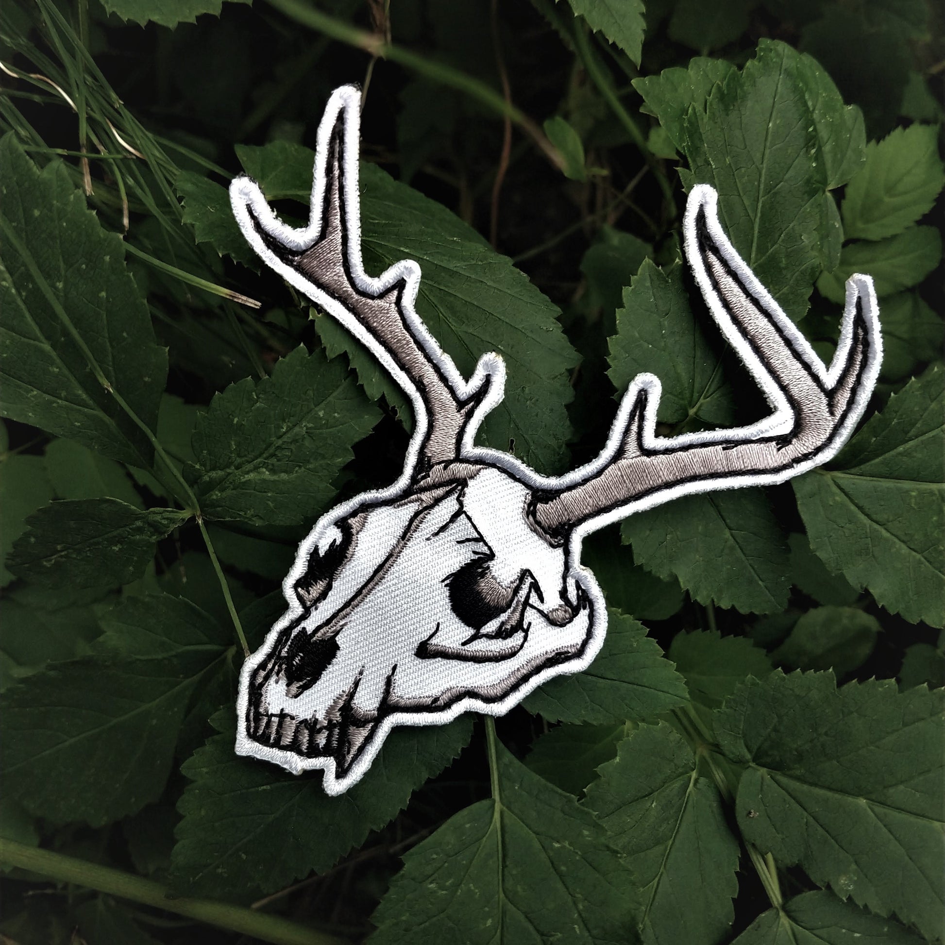 Embroidered deer skull patch on green leaves